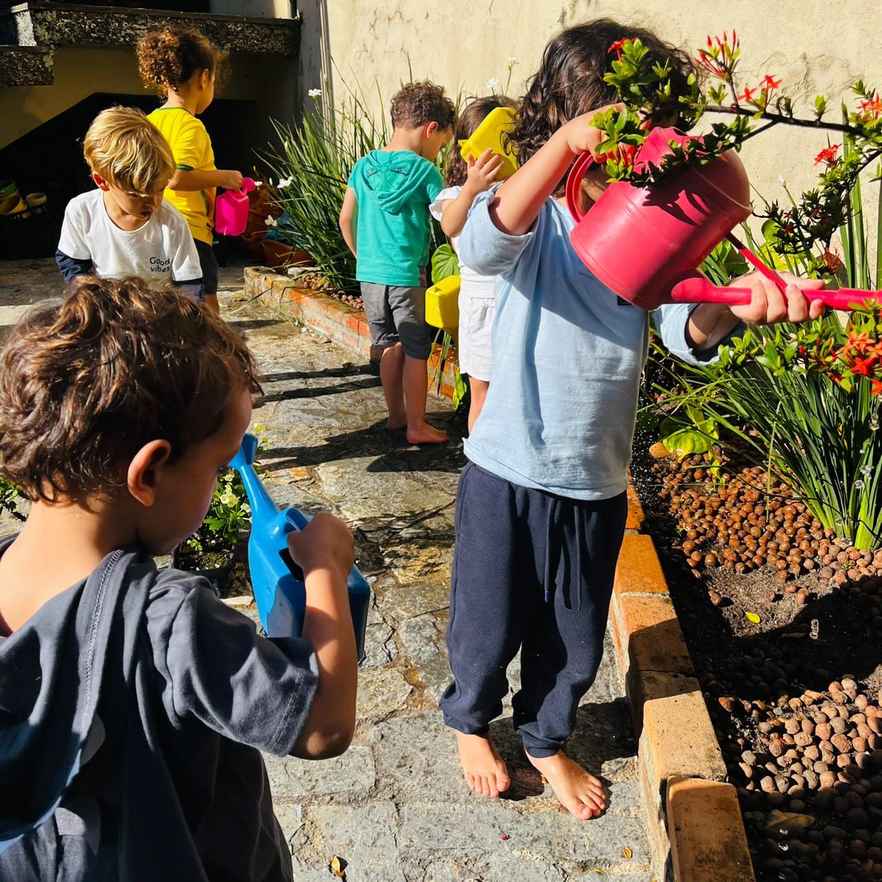 Crianças regando juntas as plantas do jardim com regadores coloridos